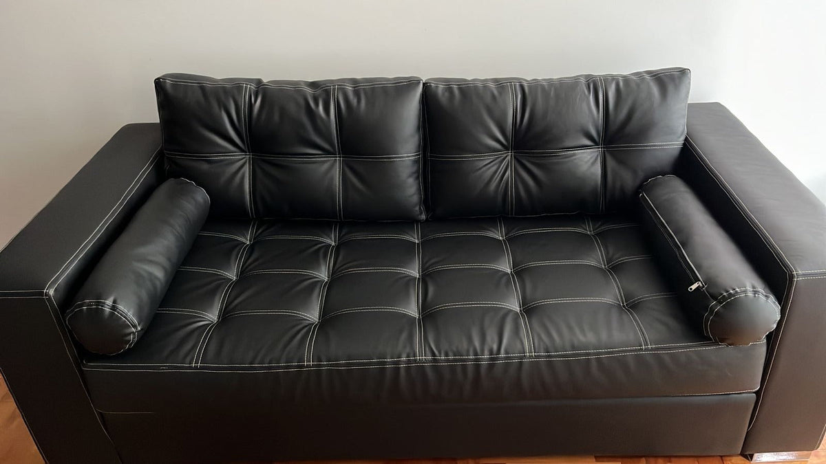 Vista frontal del sofá retapizado en cuerina Talampaya negra, con almohadones cilíndricos en los apoyabrazos
