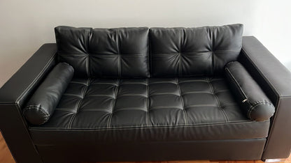 Vista frontal del sofá retapizado en cuerina Talampaya negra, con almohadones cilíndricos en los apoyabrazos