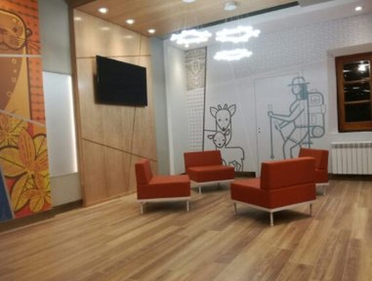 Sala de espera con sillones Janod rojos y televisor, sobre piso de madera