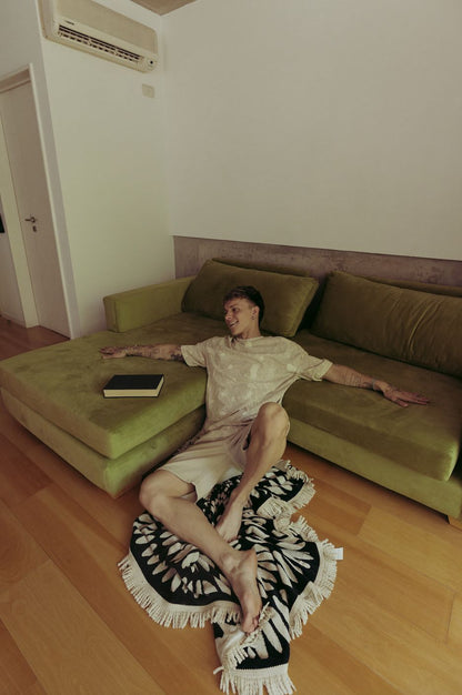 Santiago Colinet recostado sobre una alfombra frente a su Sillón Esquinero Richard verde, en el living de su casa