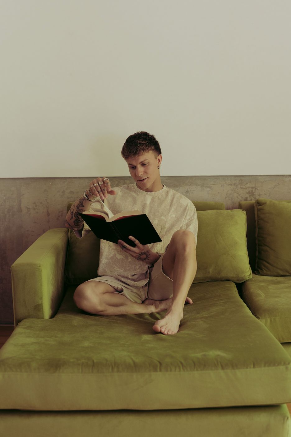 Santiago Colinet con un libro en la mano, sentado en el chaise de su Sillón Esquinero Richard verde