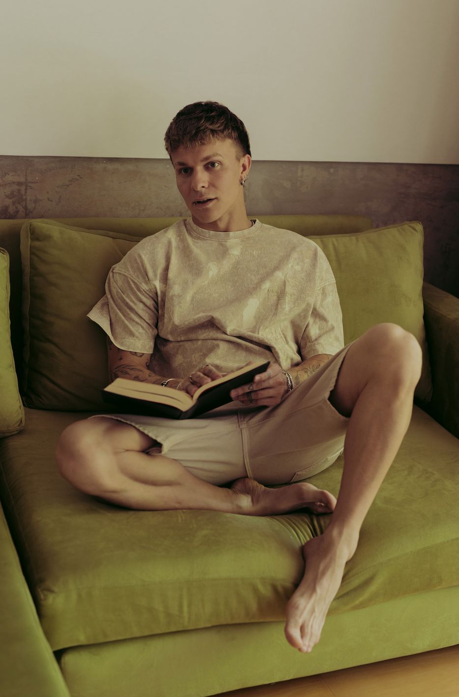 Santiago Colinet con un libro abierto, sentado de piernas cruzadas en su Sillón Esquinero Richard verde