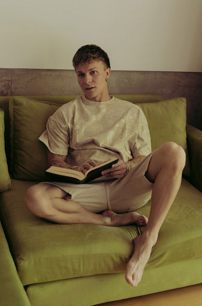 Santiago Colinet con un libro abierto, sentado de piernas cruzadas en su Sillón Esquinero Richard verde