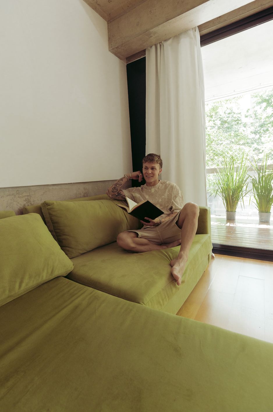Santiago Colinet leyendo en el rincón del Sillón Esquinero Richard verde, junto al ventanal con cortinas