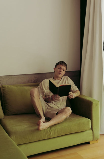 Santiago Colinet sentado con un libro en su Sillón Esquinero Richard verde, junto al ventanal