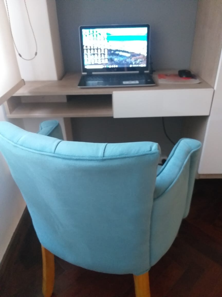Silla tipo tina en terciopelo turquesa con patas de madera, frente al escritorio del home office de Candela