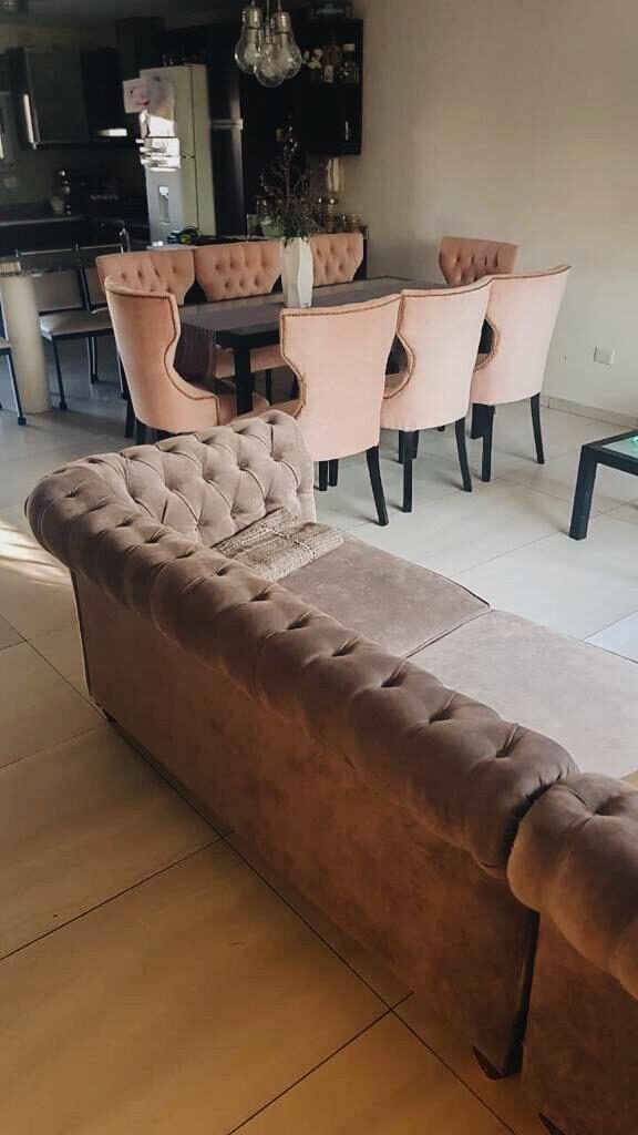 Sillas Menphis rosa con capitoné y tachas en el comedor de Lucía, con un sofá Chesterfield crema al fondo
