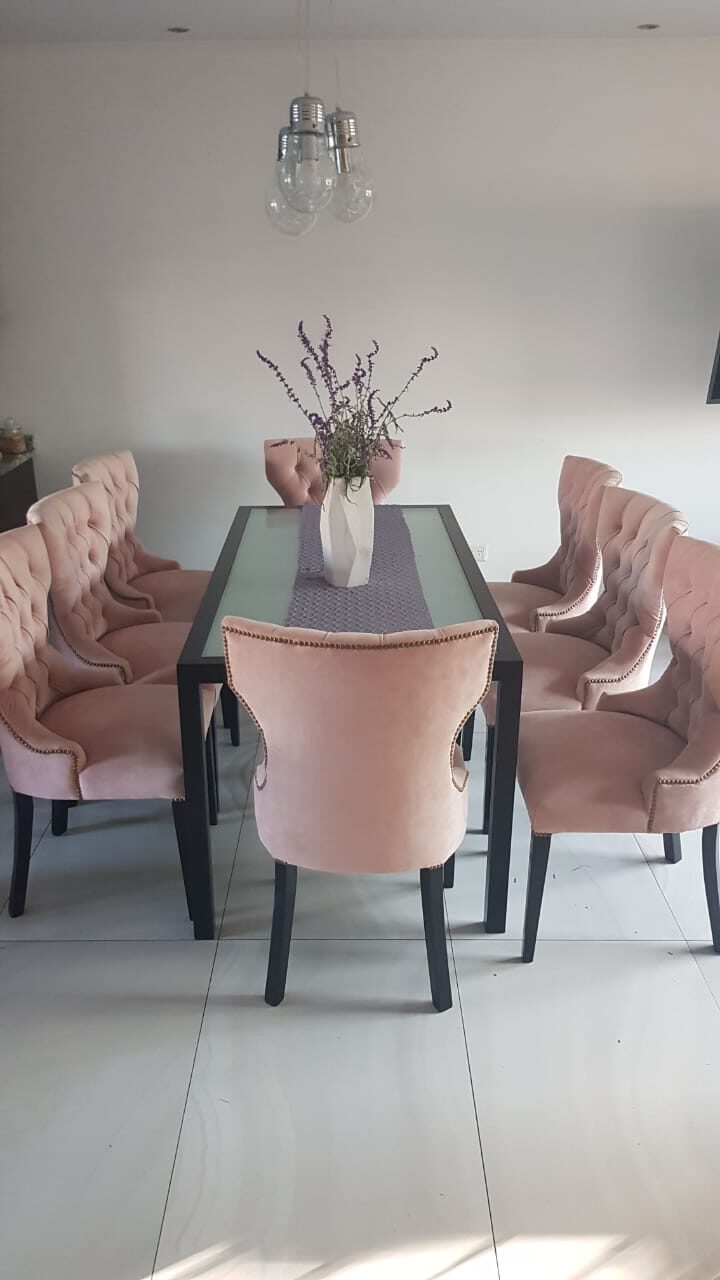 Seis Sillas Menphis rosa capitoné alrededor de la mesa de vidrio con estructura negra del comedor de Lucía