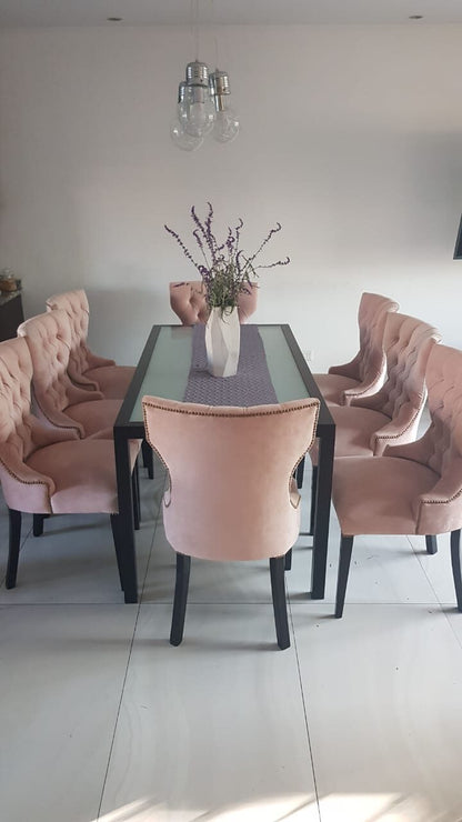 Seis Sillas Menphis rosa capitoné alrededor de la mesa de vidrio con estructura negra del comedor de Lucía