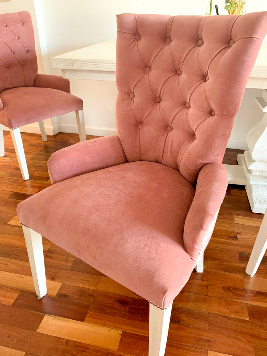 Sillas Menphis en velvet rosa con respaldo capitoné, apoyabrazos, tachas y patas blancas, en el comedor de Lourdes sobre parquet