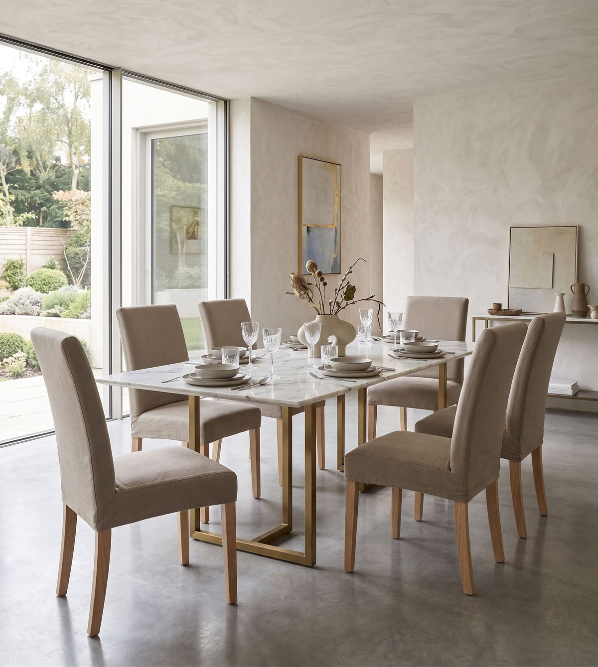 Sillas Vestida en beige alrededor de una mesa de mármol con base dorada, en un comedor luminoso