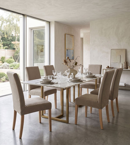 Sillas Vestida en beige alrededor de una mesa de mármol con base dorada, en un comedor luminoso