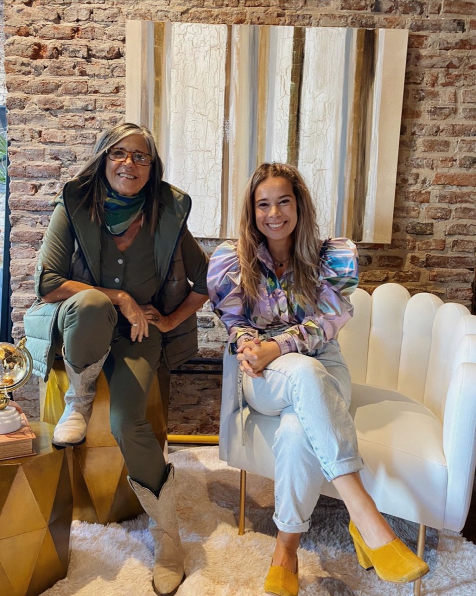 Clienta posando junto al Sillón Angie tapizado en blanco, living de estilo ecléctico con pared de ladrillo visto — tapizado a medida