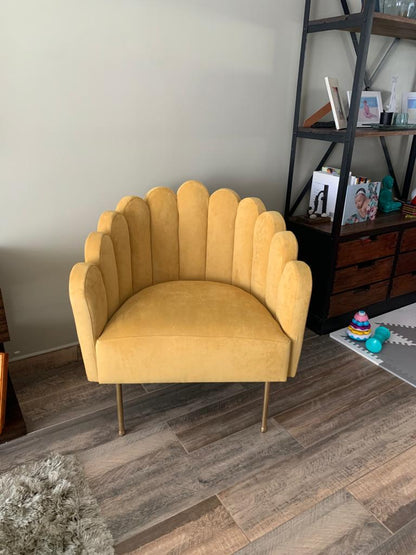 Sillón Angie mostaza con respaldo acanalado en forma de concha y patas doradas, junto a la biblioteca de Yamila