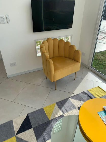 Sillón Angie mostaza con respaldo en forma de concha, junto al ventanal del loft de Austral Rental