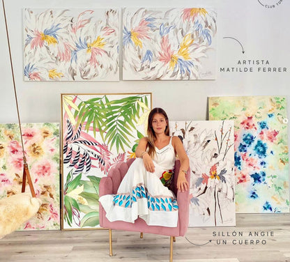 La artista Matilde Ferrer sentada en su Sillón Angie rosa, rodeada de sus cuadros de flores y hojas tropicales