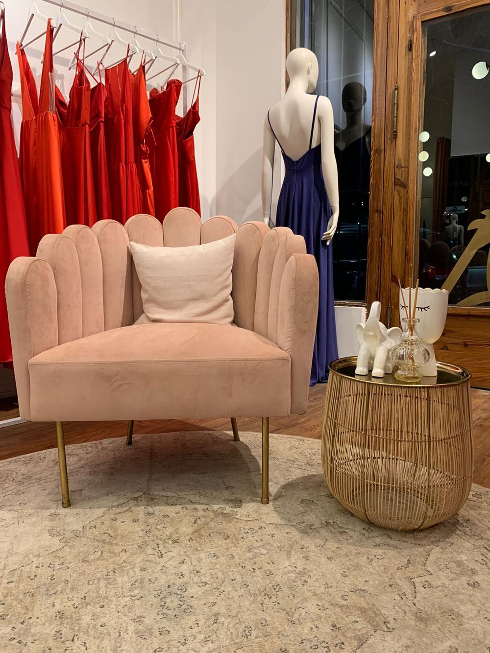 Sillón Angie rosa con respaldo de pétalos y patas doradas junto a un perchero de vestidos en el local de Natalia Oreiro