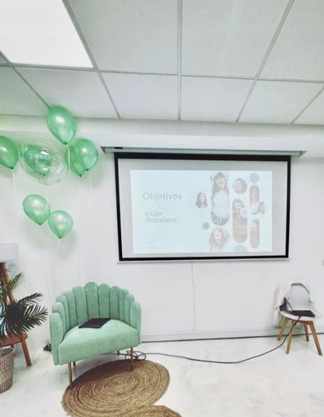 Sillón Angie verde menta con patas doradas frente a la pantalla de proyección en la sala de encuentros de Mujer Financiera