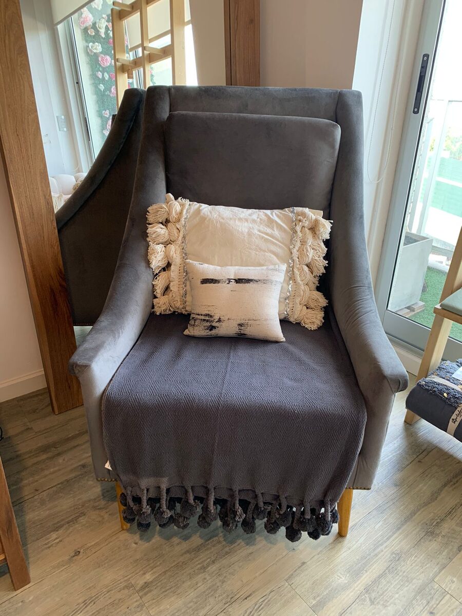 Sillón Bélgica gris con manta de pompones y almohadones en el rincón de lectura de Roxana