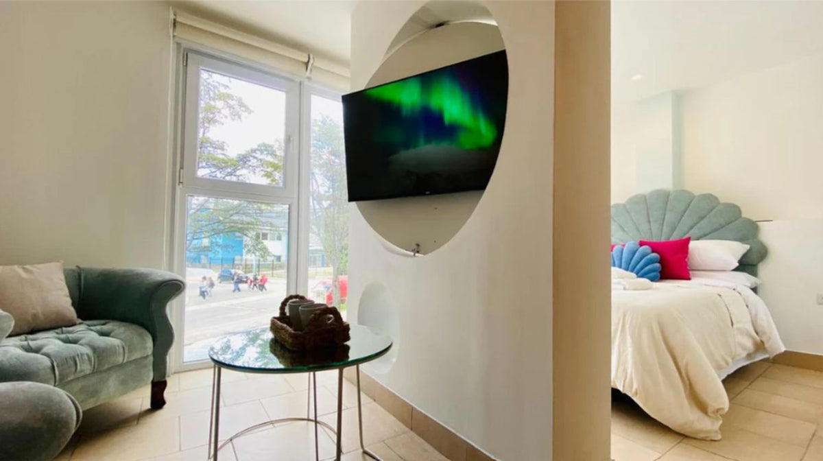 Vista completa del ambiente: sillón Brigitte celeste junto al ventanal y, del otro lado del tabique, la cama con el respaldo Ostras