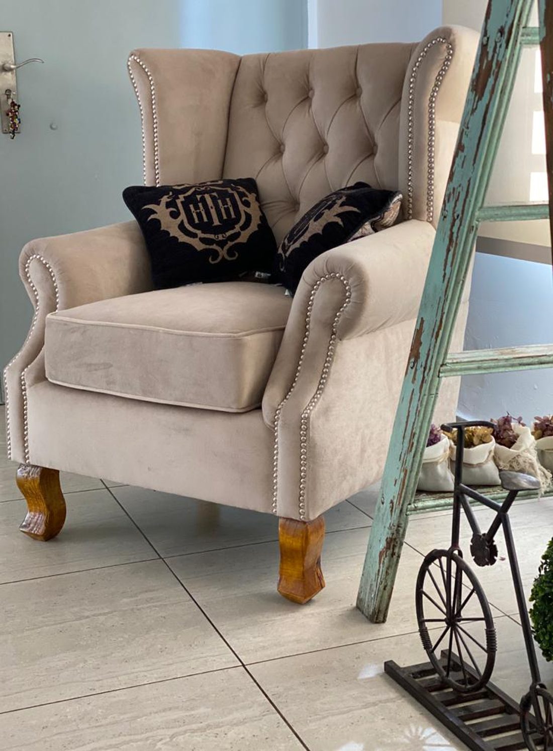 Sillón Elepant claro con respaldo capitoné, orejas y tachas plateadas, junto a una escalera de madera decorativa en el dúplex de Daniela en Adrogué