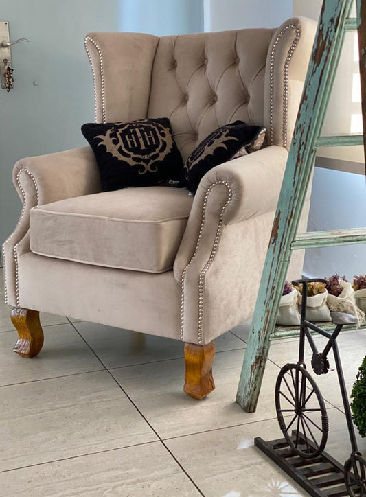 Sillón Elepant gris perla con respaldo capitoné, orejas y tachas plateadas, junto a una escalera de madera decorativa en el dúplex de Daniela en Adrogué