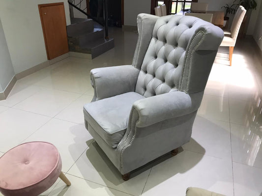 Sillón Elepant gris con capitoné y tachas plateadas junto a la chimenea de piedra, en el living de Sabrina