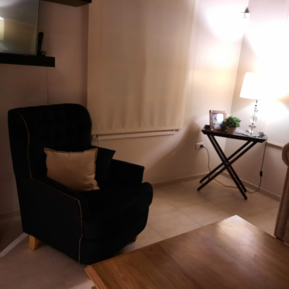 Sillón Esmeralda negro con almohadón beige, frente a la mesa de madera del living de Rocío