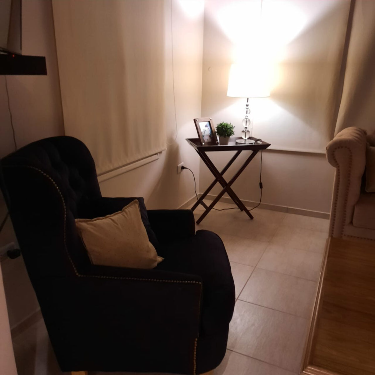 Sillón Esmeralda negro con capitoné y tachas doradas, junto al apoyabrazos de un Chesterfield beige, en el living de Rosana