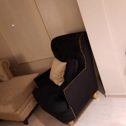 Vista lateral del Sillón Esmeralda negro con borde de tachas, junto al chaise del Esquinero Chesterfield de Rocío