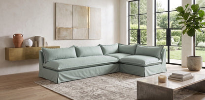 Sillón esquinero Tassa con funda de tussor gris claro en un living con ventanal y mesa ratona de piedra