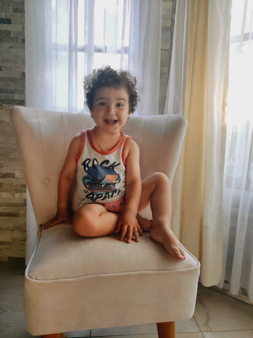 Nena sentada en un Sillón Matero Alpes crema, con respaldo acanalado y patas de madera, junto a una ventana