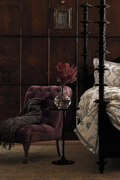 Sillón Matero Oriana bordó junto a una cama con columnas de madera oscura
