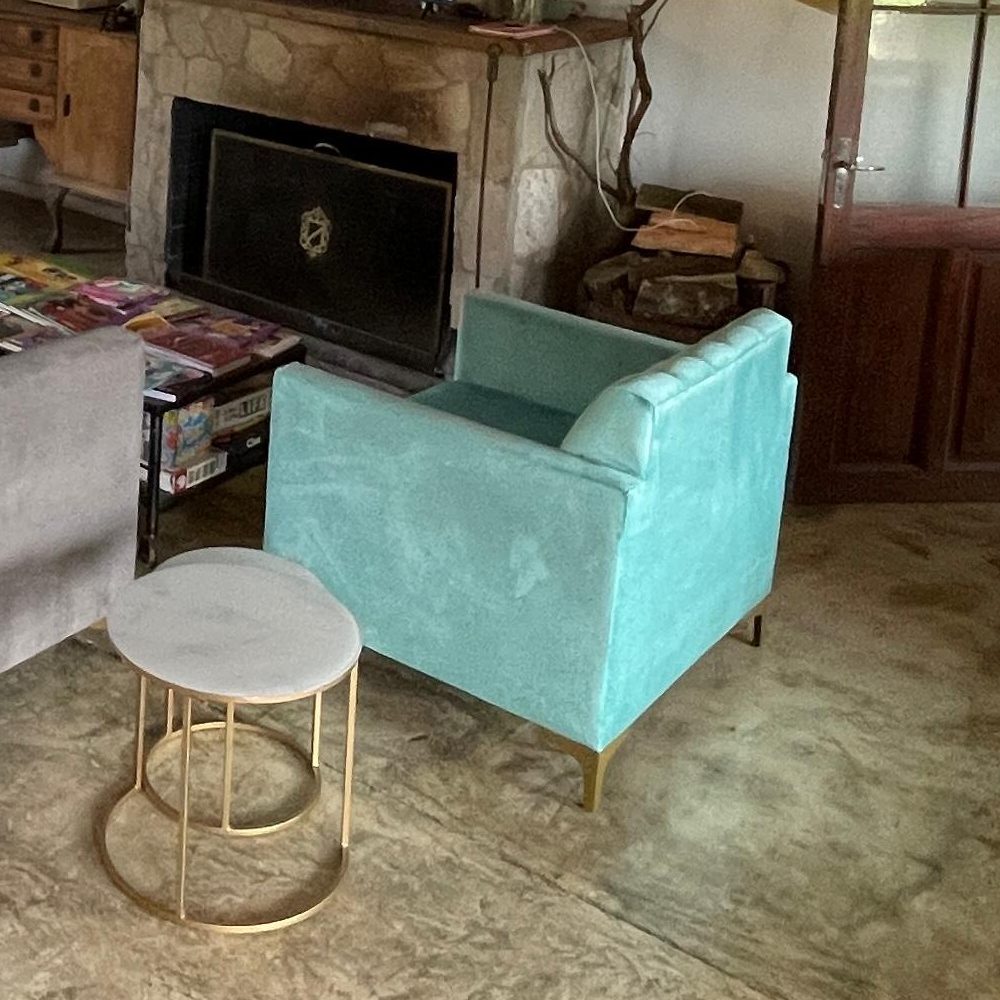 Detalle del Sillón Mila turquesa con patas doradas junto al hogar de piedra en la casa de Josefina, Esteros del Iberá