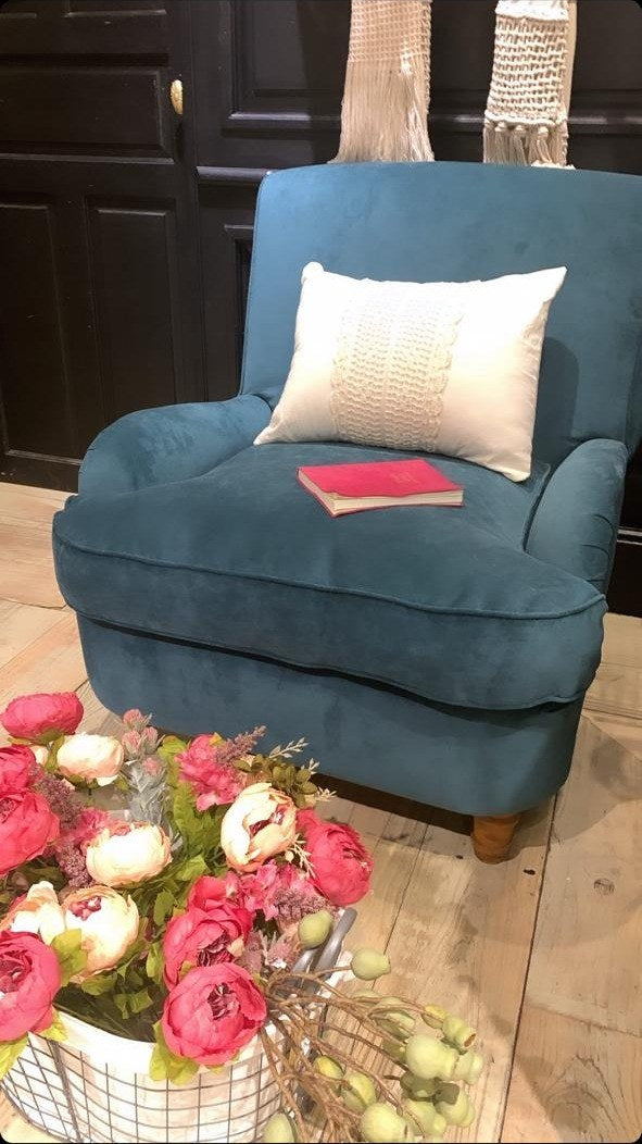 Sillón Minerva tapizado en pana azul petróleo, con almohadón crudo y un ramo de flores, en el living de Martín