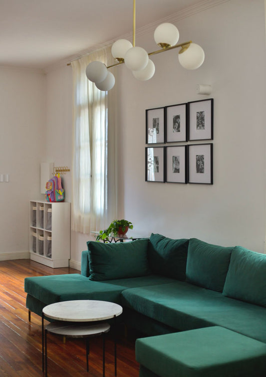 Sillón en forma de herradura tapizado en tela verde oscuro, con cojines a juego, ubicado en una sala con piso de madera y mesas de centro redondas con superficie de mármol