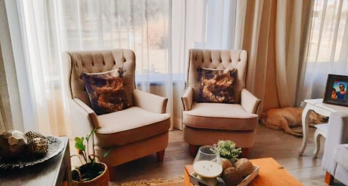 Dos Sillones Esmeralda beige con capitoné y tachas, enfrentados en el rincón de lectura junto al ventanal