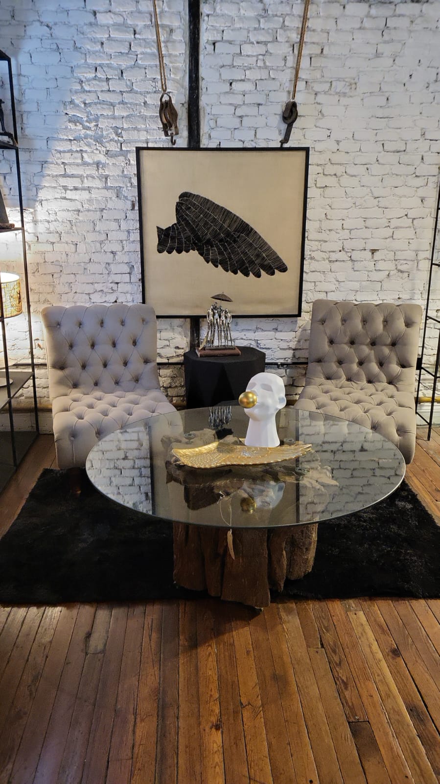 Dos Sillones Matero Oriana gris claro con capitoné y sin apoyabrazos, frente a una mesa de vidrio y una pared de ladrillo blanco