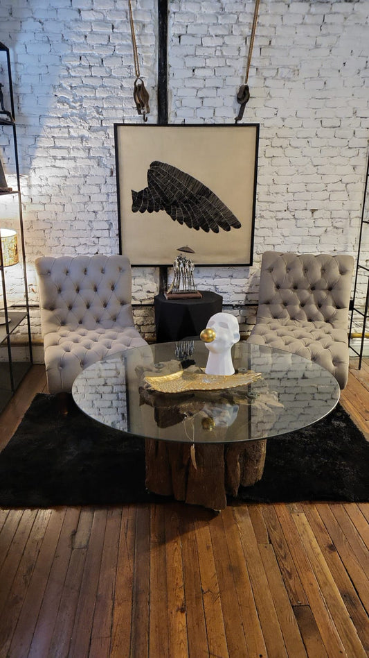 Dos Sillones Matero Oriana gris claro con capitoné y sin apoyabrazos, frente a una mesa de vidrio y una pared de ladrillo blanco
