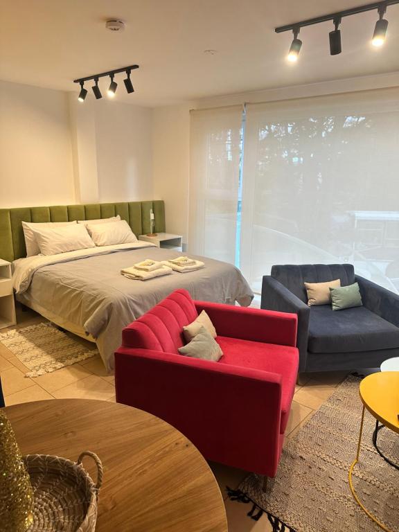 Sillones Mila rojo y azul junto a una mesa auxiliar amarilla, con el Respaldo Alpes verde de fondo