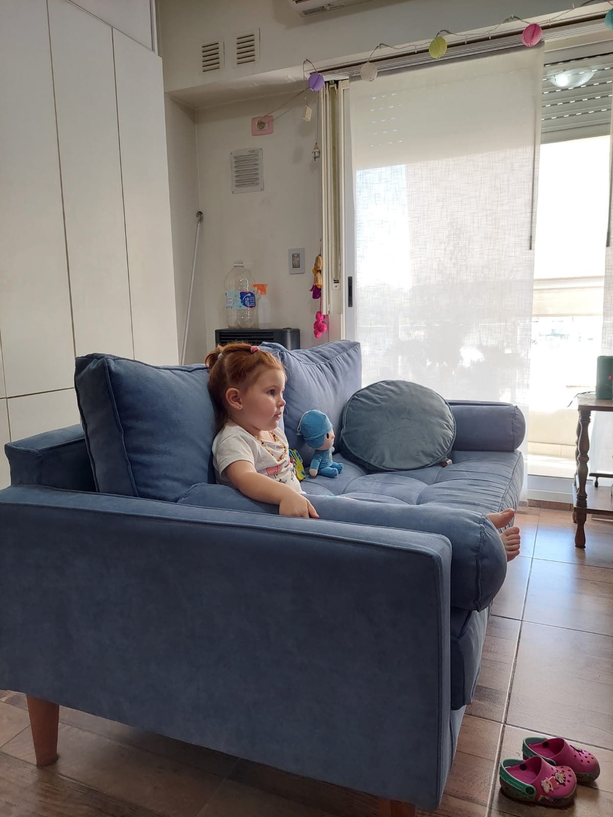 Hija de Romina sentada en el Bambú azul, con almohadón cilíndrico en el brazo y patas de madera, en su casa
