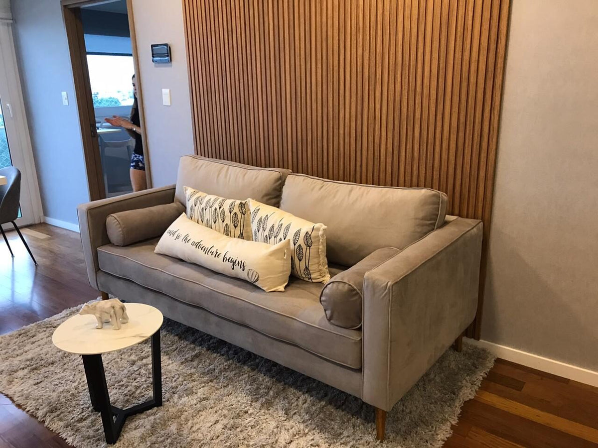 Sofá Bambú beige con almohadones cilíndricos en los brazos, frente a una pared de varillado de madera natural, en el living de Denise
