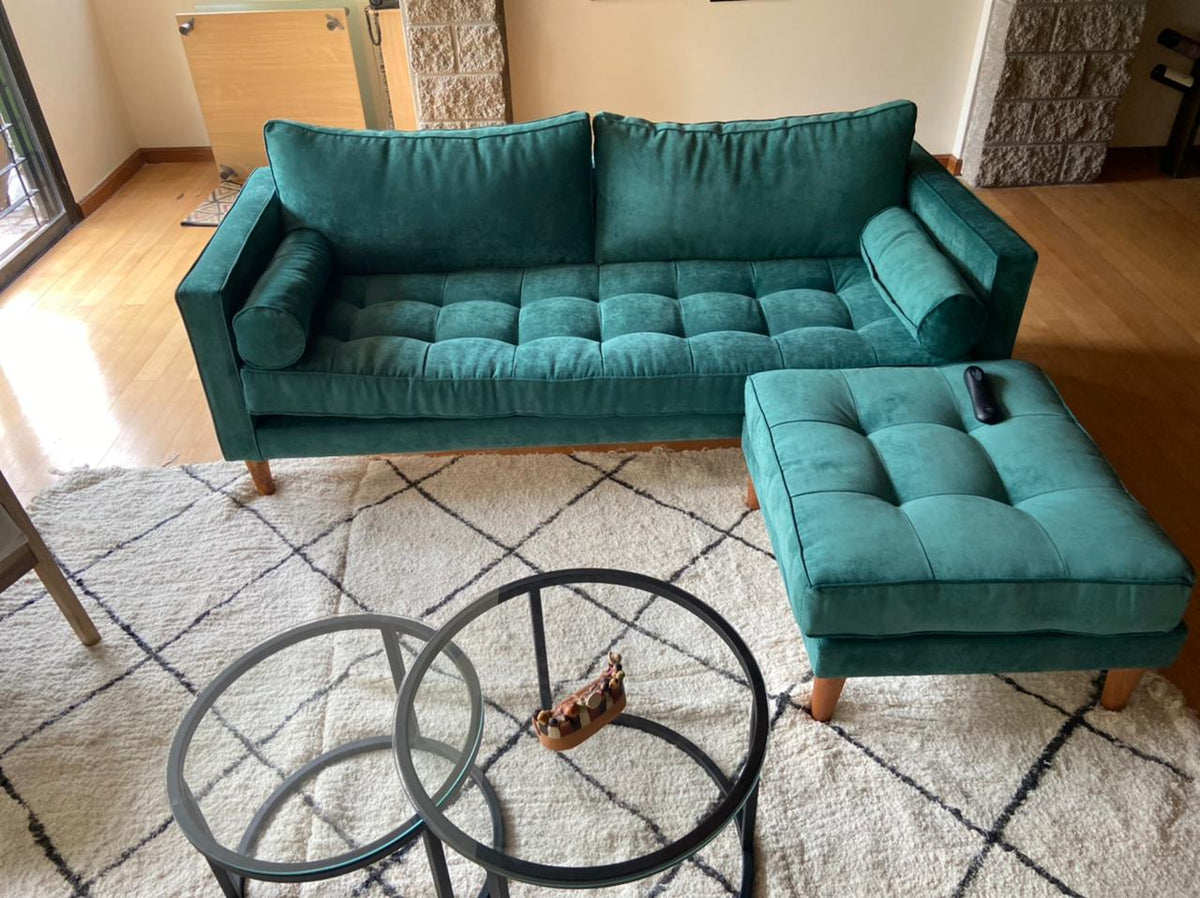 Sofá Bambú verde inglés con botoné, almohadones cilíndricos y puff suelto al tono, en el living de Malena