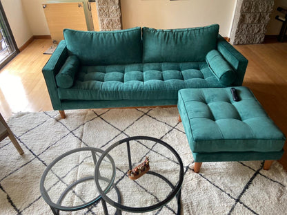 Sofá Bambú verde inglés con botoné, almohadones cilíndricos y puff suelto al tono, en el living de Malena