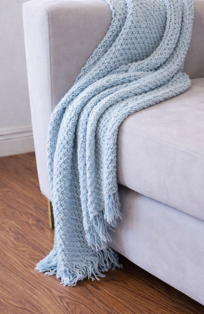 Detalle del apoyabrazos del Sofá Bélgica gris con una manta celeste tejida, en el living de Pipo
