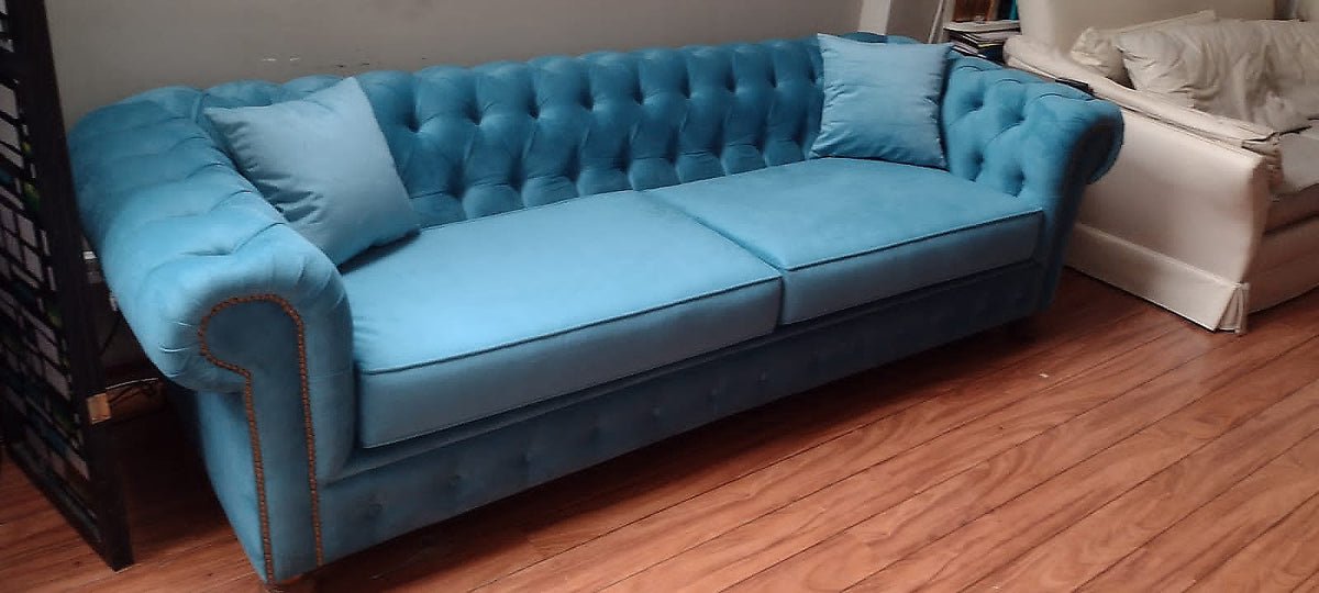 Sofá Chesterfield de 3 cuerpos en terciopelo azul turquesa, con capitoné y tachas cobre en el apoyabrazos, en el living de Valentina