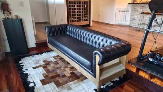 Sofá Deconstructed en cuerina Talampaya negra con capitoné profundo y base de madera semi-vista, en el living minimalista de Emilia