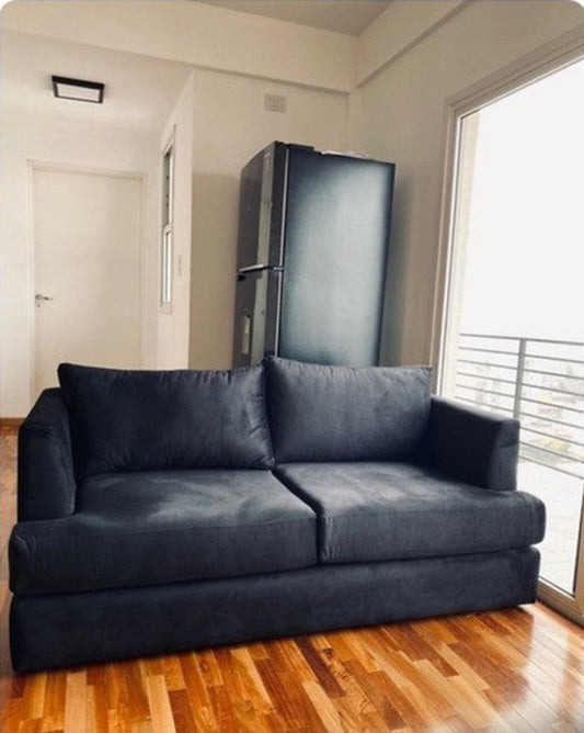 Sofá de dos cuerpos a medida tapizado en negro de Nahuel, en su living con balcón y piso de madera