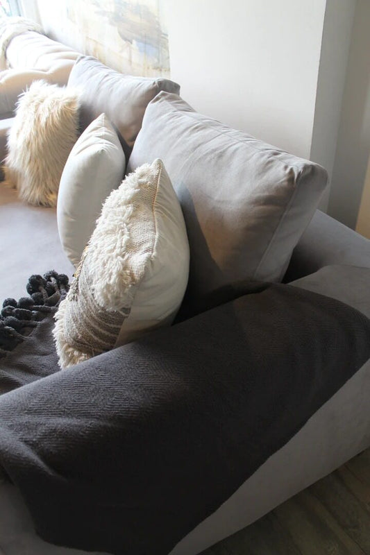 Sofá Elton gris con almohadones de lana y pelo y una manta con pompones, en el living boho de Silvana