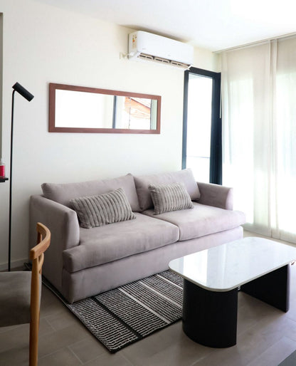 Sofá Elton gris lila con almohadones acanalados, mesa de centro de mármol y alfombra rayada, en el living de WN Interiores
